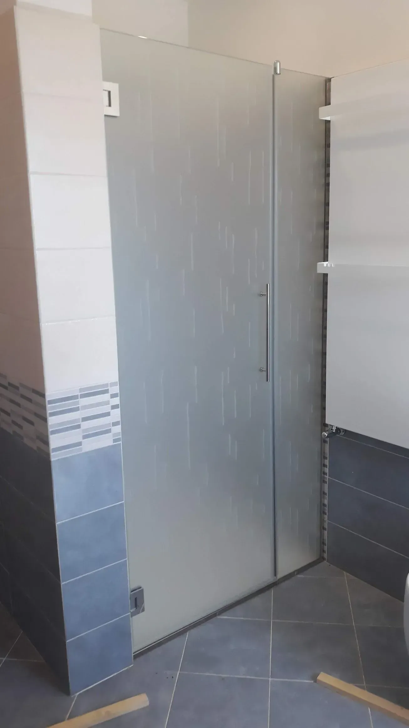 Porta grigia parzialmente aperta in un bagno o spogliatoio piastrellato.