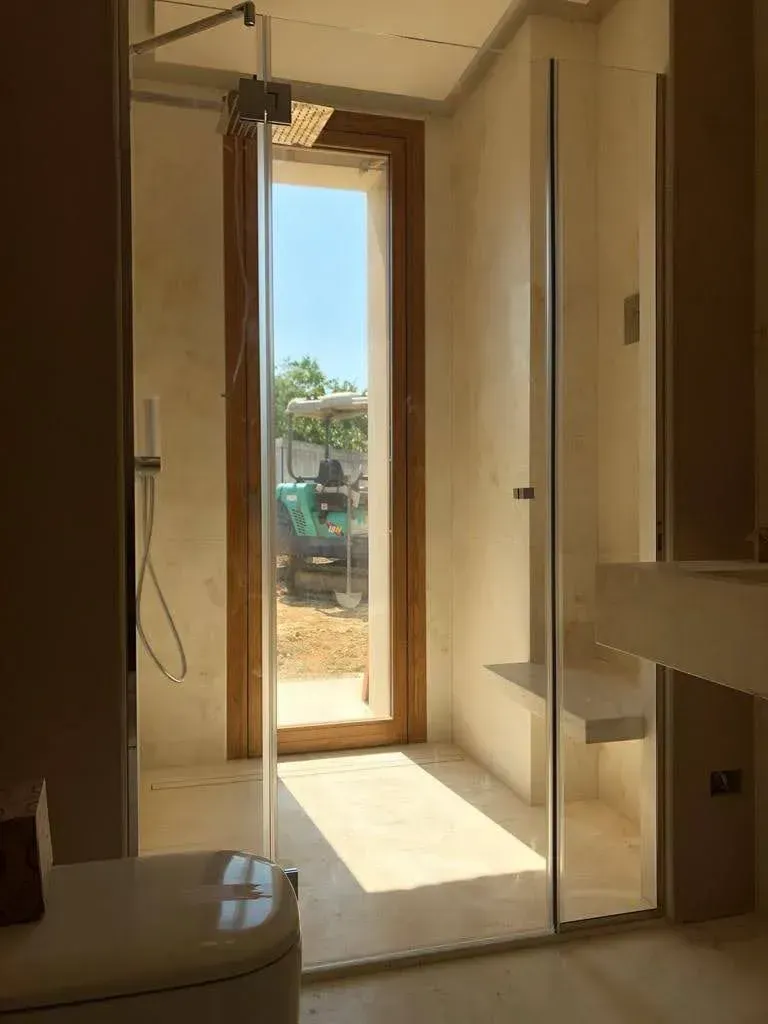 Corridoio incompiuto e illuminato dal sole, con porta aperta che dà su un cantiere edile esterno.