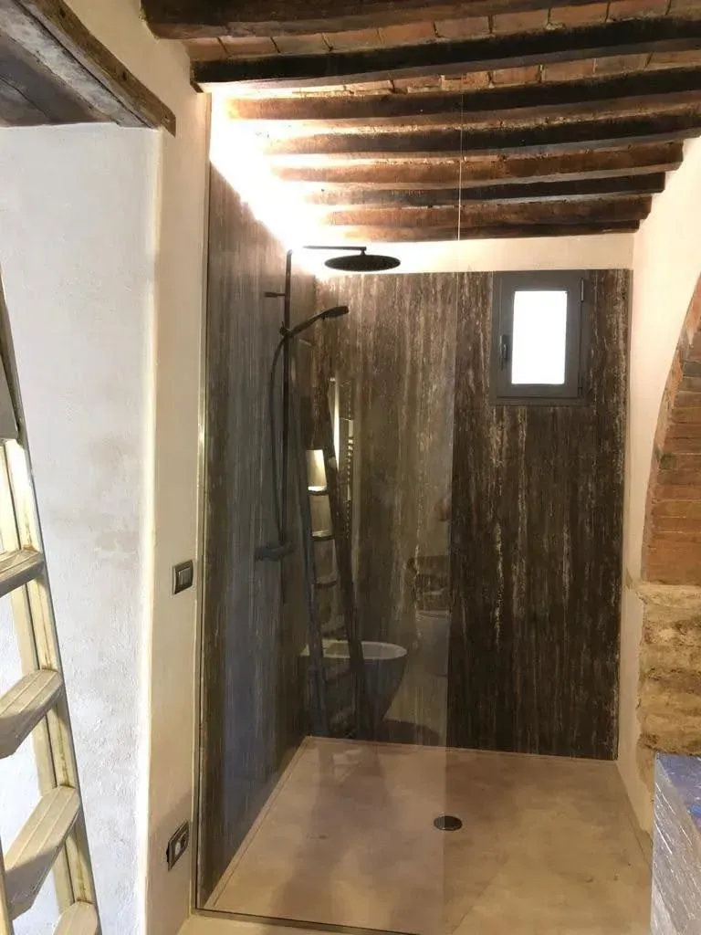 Stretto corridoio rustico con travi a vista sul soffitto, box doccia in vetro sulla sinistra e porta in legno in fondo.