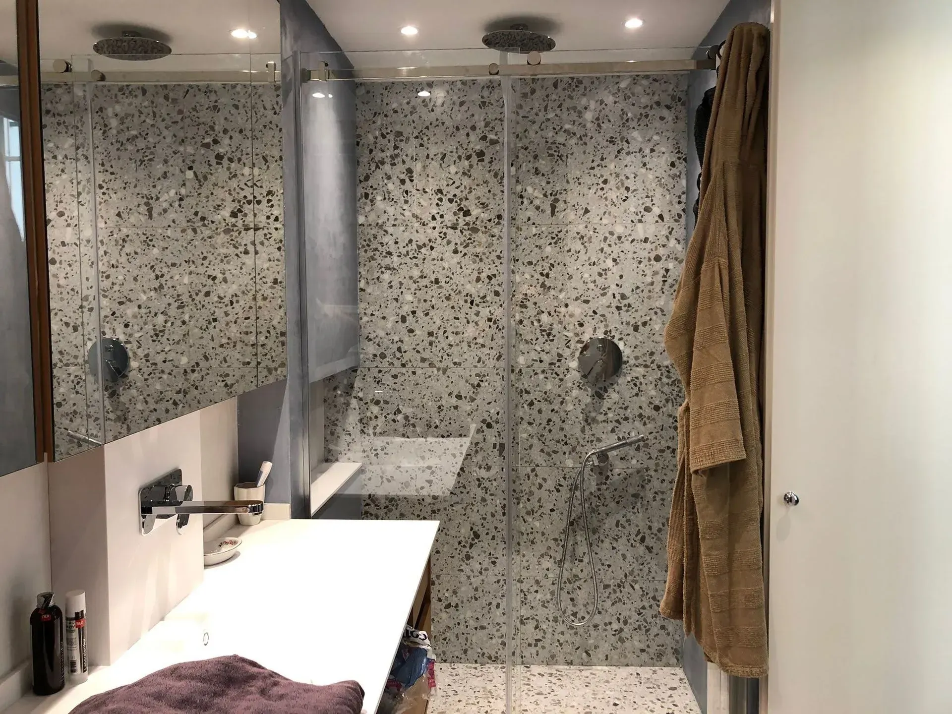 Bagno moderno con doppio lavabo, ampi specchi, doccia rivestita in piastrelle di pietra e portasciugamani appeso.