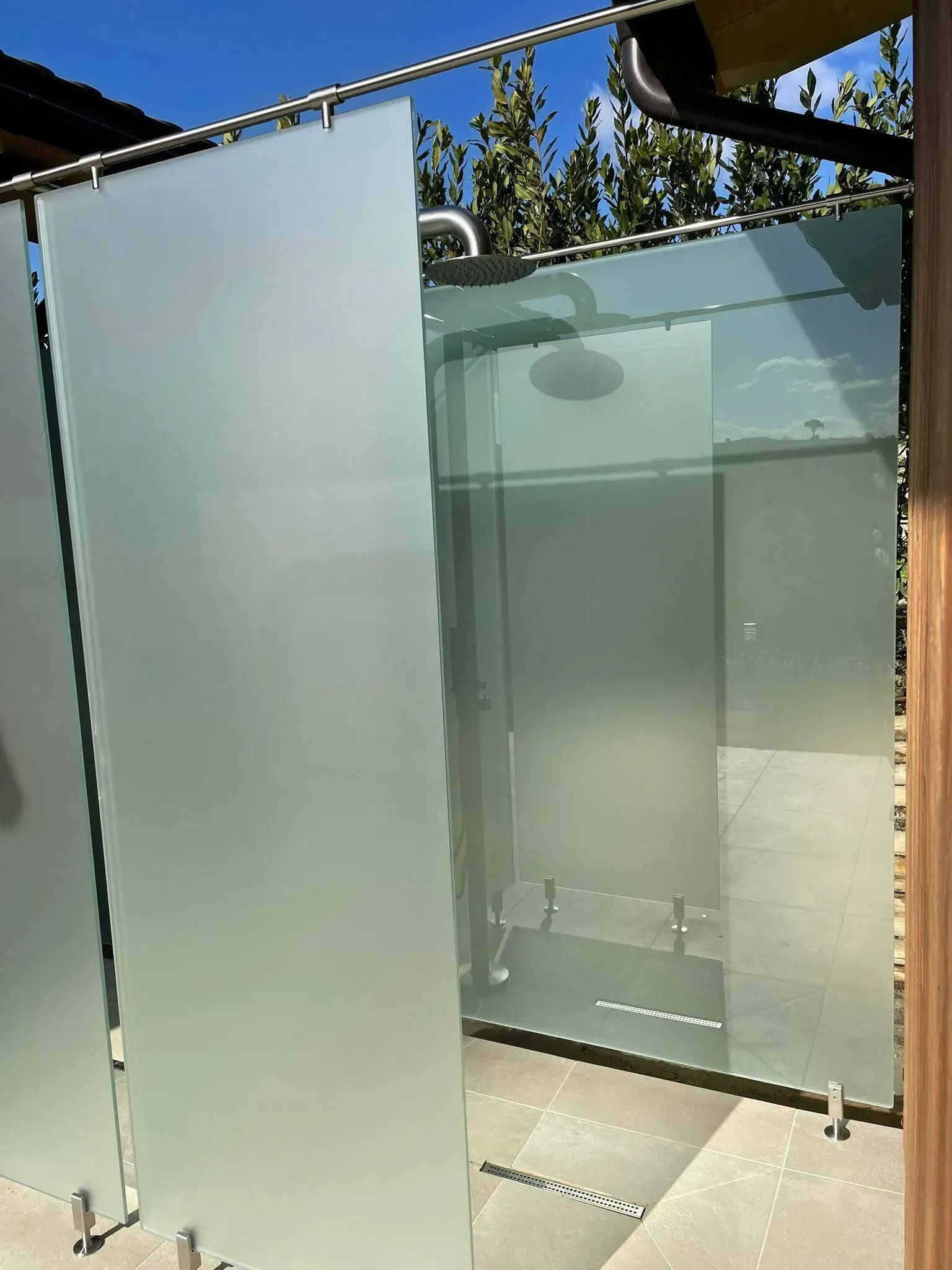 Box doccia in vetro satinato con porta a battente trasparente, in un ambiente esterno soleggiato.