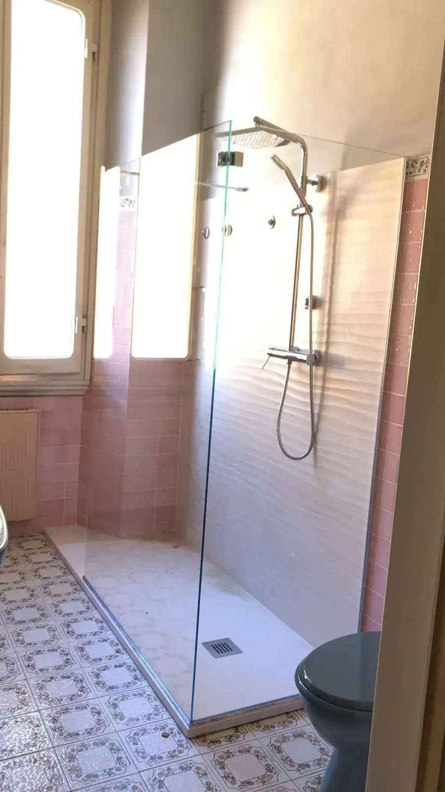 Bagno moderno con cabina doccia bianca, pareti piastrellate e pavimento piastrellato con motivi decorativi vicino a una finestra.