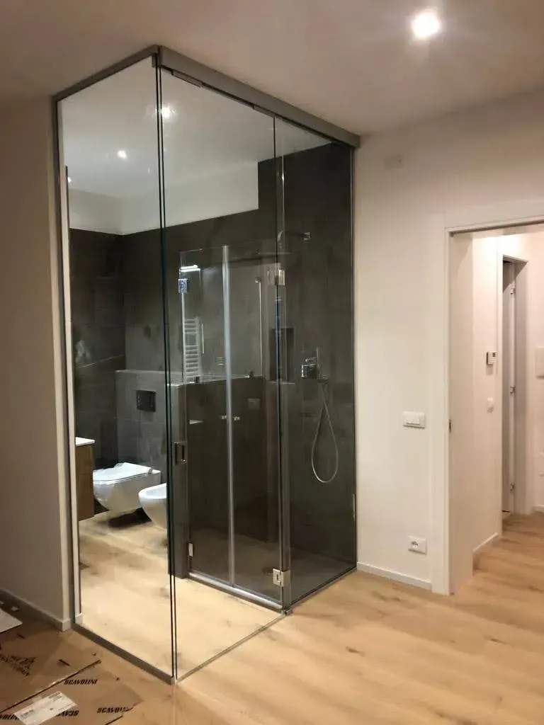 Bagno moderno con doccia con box in vetro, pareti rivestite con piastrelle scure e pavimento in legno chiaro.