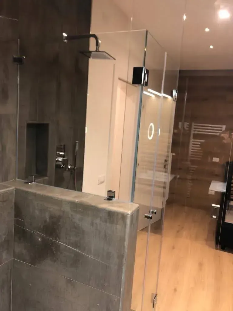 Bagno moderno con box doccia in vetro, pareti rivestite con piastrelle scure e pavimento in legno chiaro.