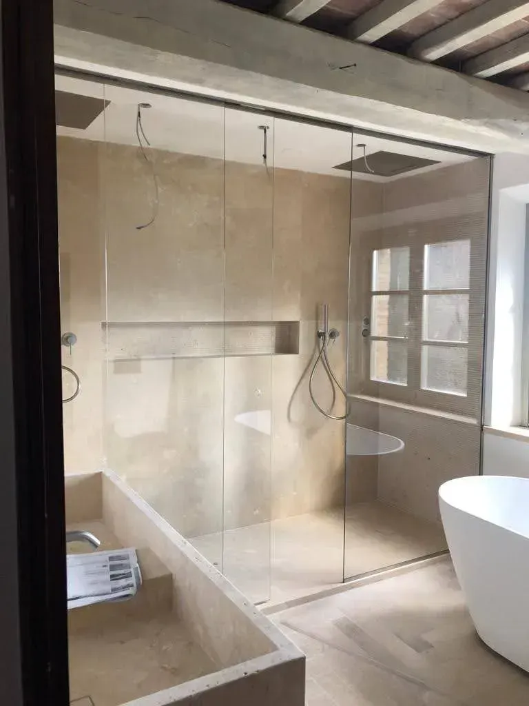 Bagno moderno con box doccia in vetro, piastrelle beige e vasca freestanding accanto a una finestra.