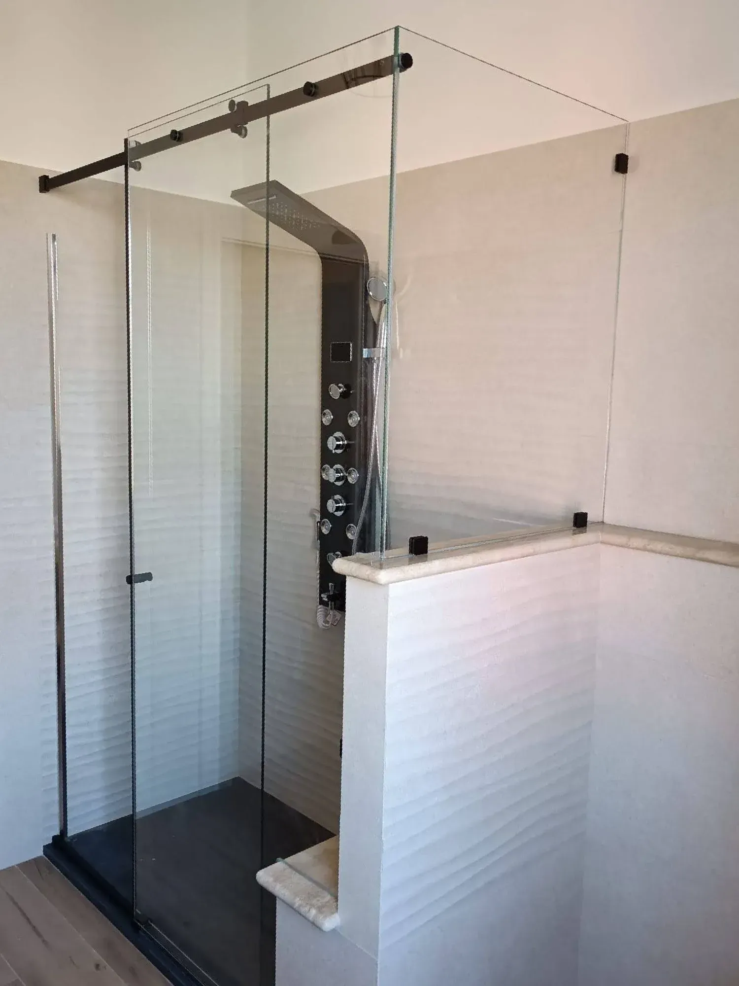 Doccia con box in vetro, rubinetteria nera e mezza parete rivestita di piastrelle bianche in un bagno.