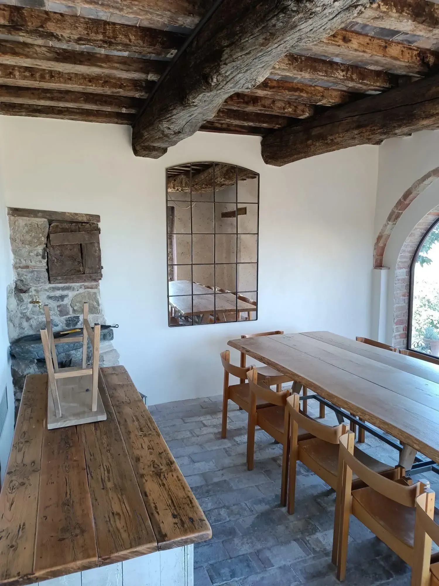 Sala da pranzo rustica con tavoli e sedie in legno e soffitto con travi a vista in un interno luminoso