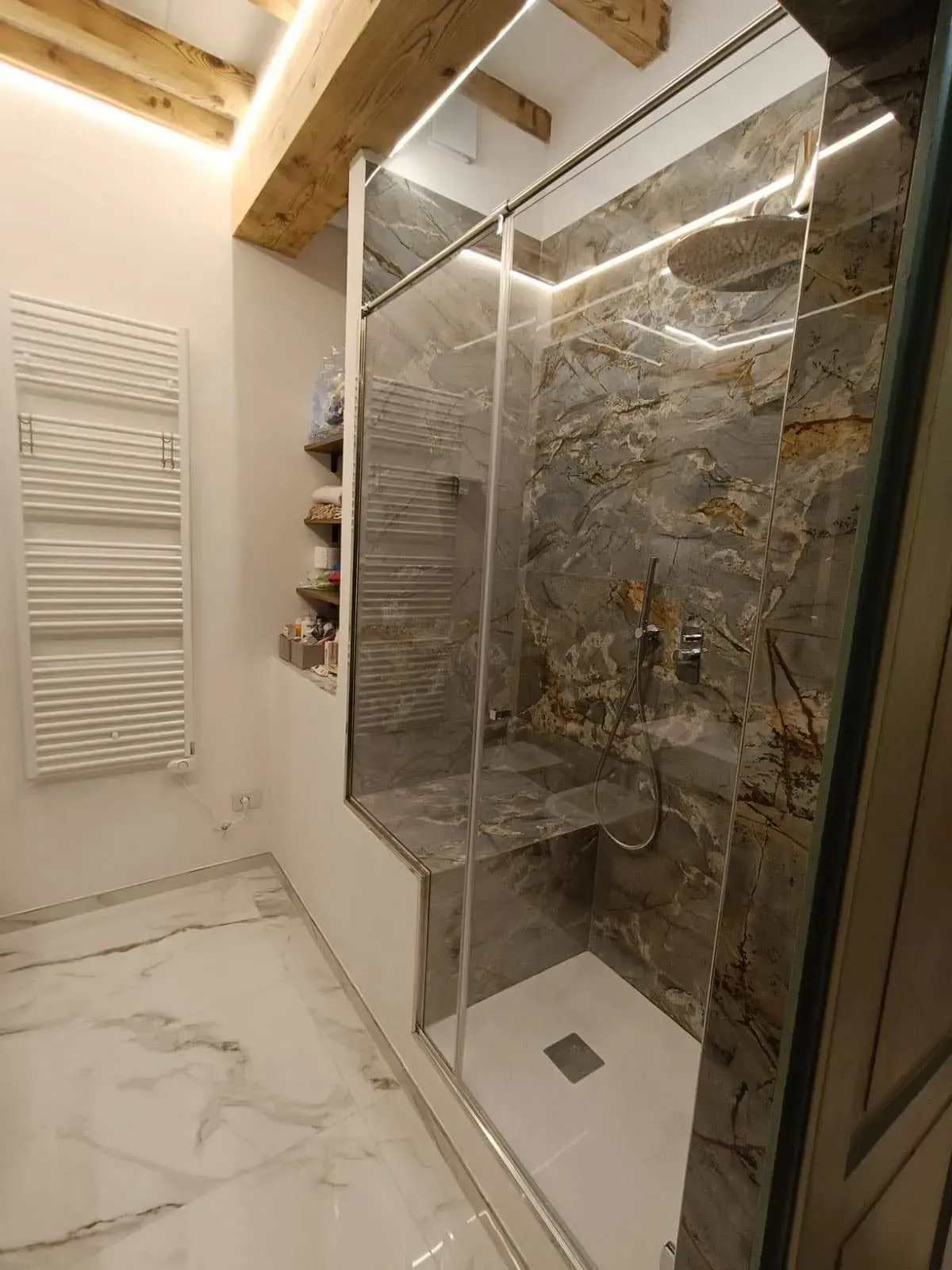 Bagno moderno con doccia in marmo, box doccia in vetro e travi a vista sul soffitto.