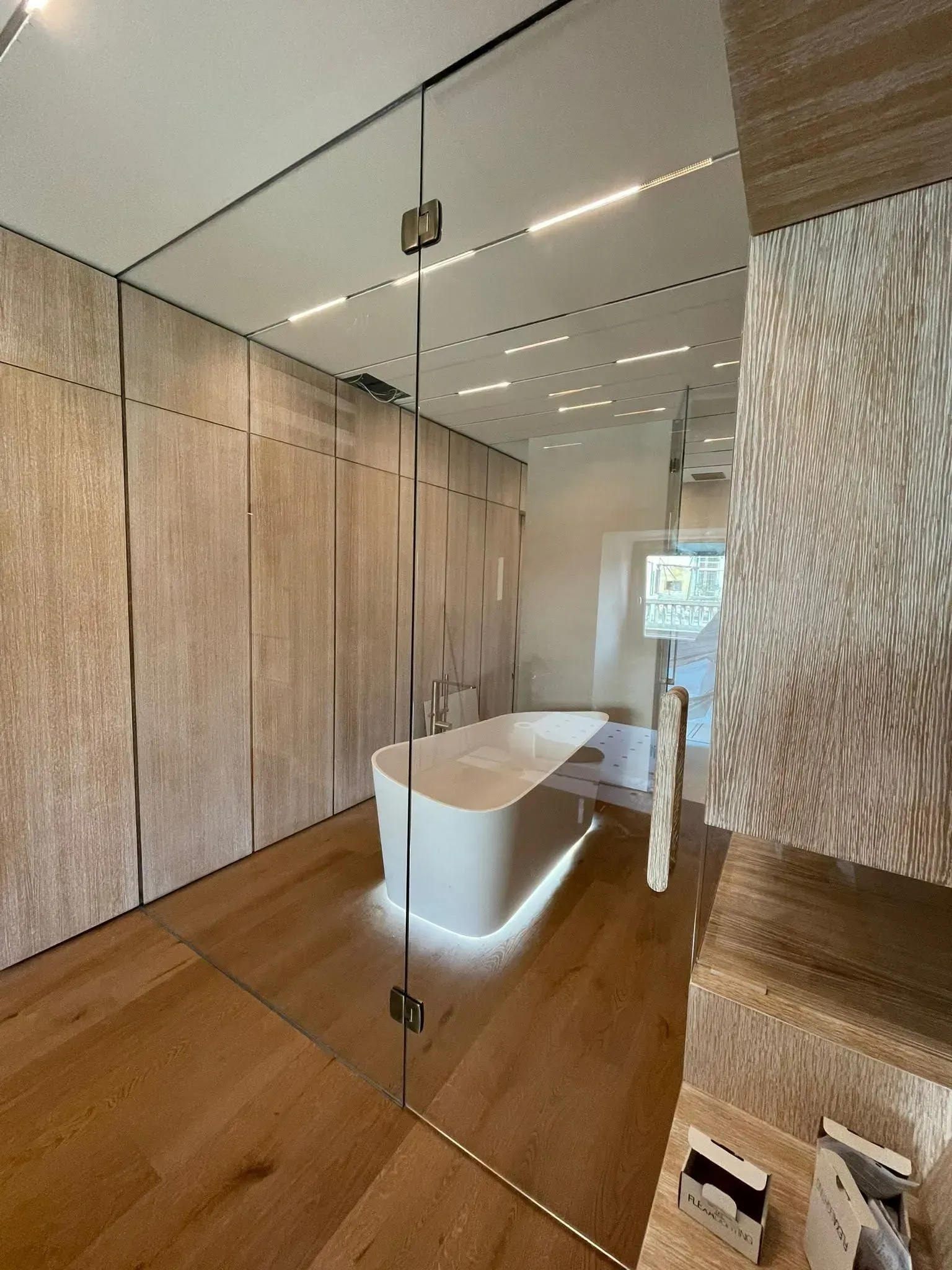Hall moderna con pareti in legno, soffitto a specchio, bancone della reception bianco e pavimento retroilluminato con luce calda.