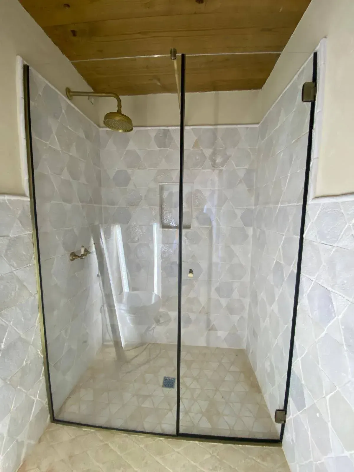 Box doccia con pareti in vetro, rivestimento in piastrelle, pavimento beige e soffitto in legno.