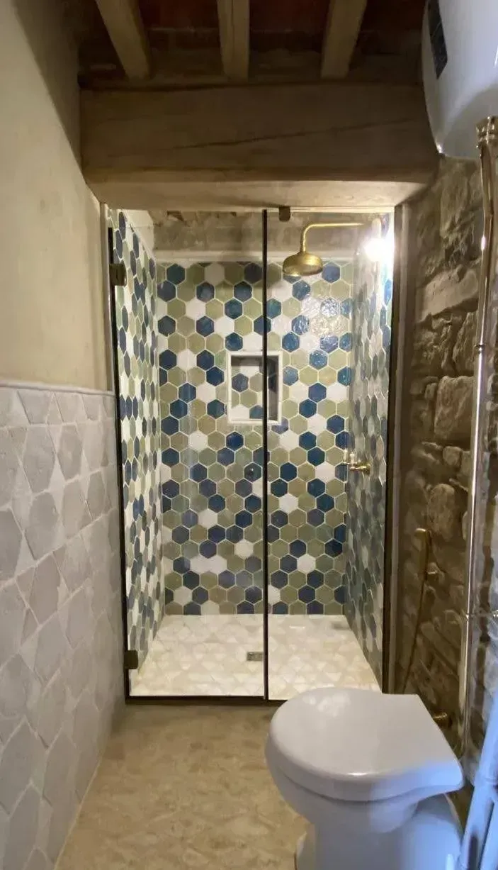Piccolo bagno con box doccia in vetro, piastrelle blu decorate e WC in primo piano.