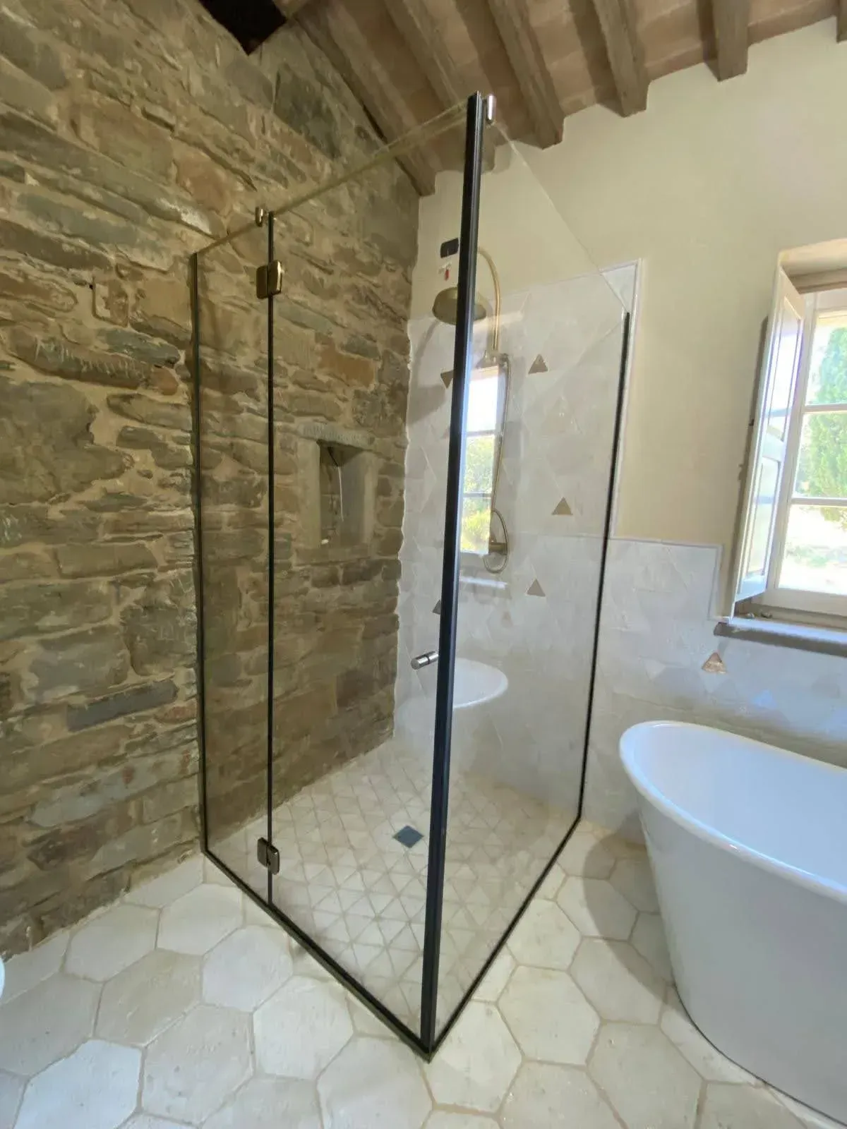 Bagno moderno con doccia in vetro, parete in pietra, vasca bianca e piastrelle esagonali sul pavimento.