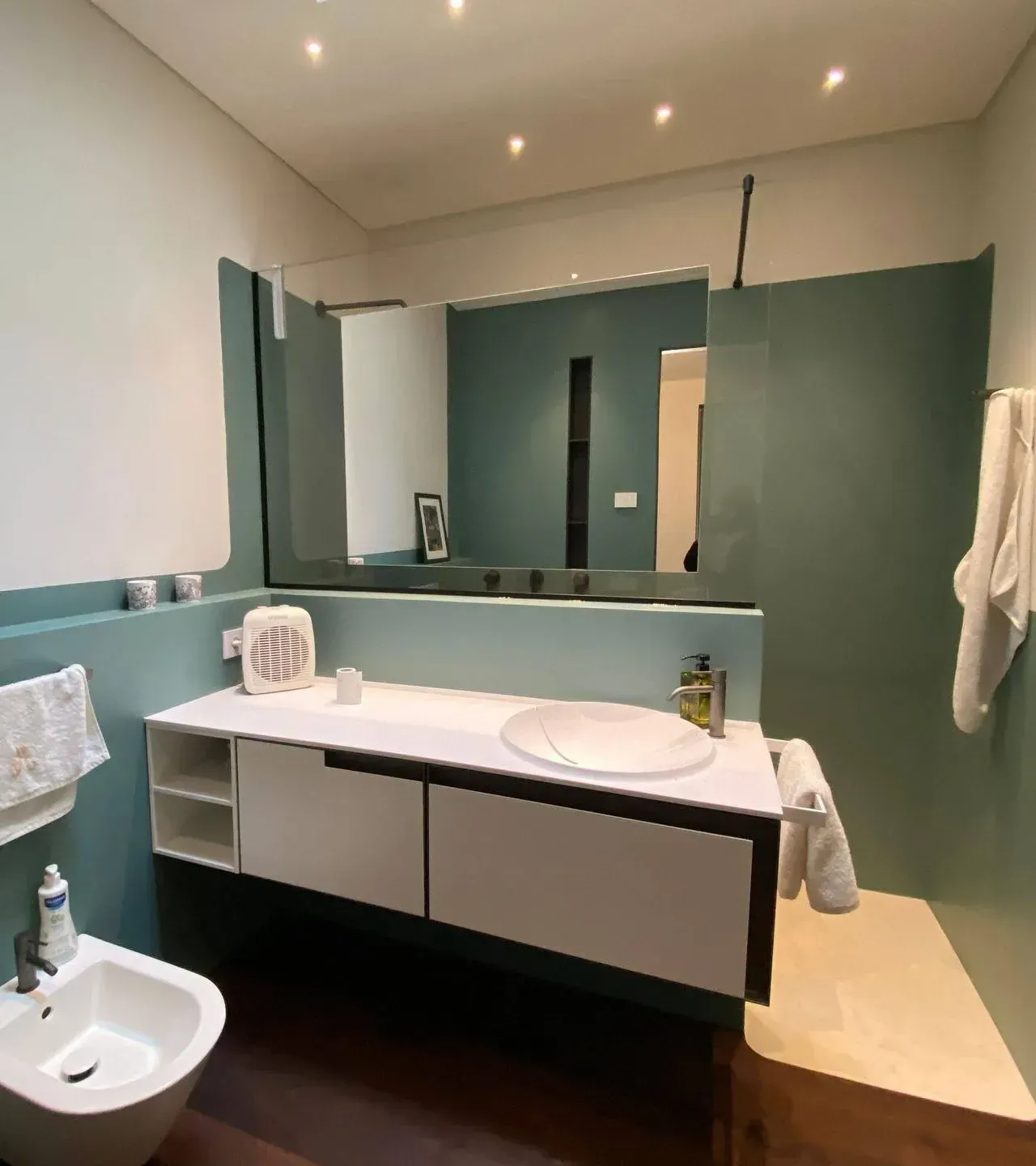 Bagno moderno con pareti color verde acqua, mobile lavabo bianco, ampio specchio, lavandino e cabina doccia.