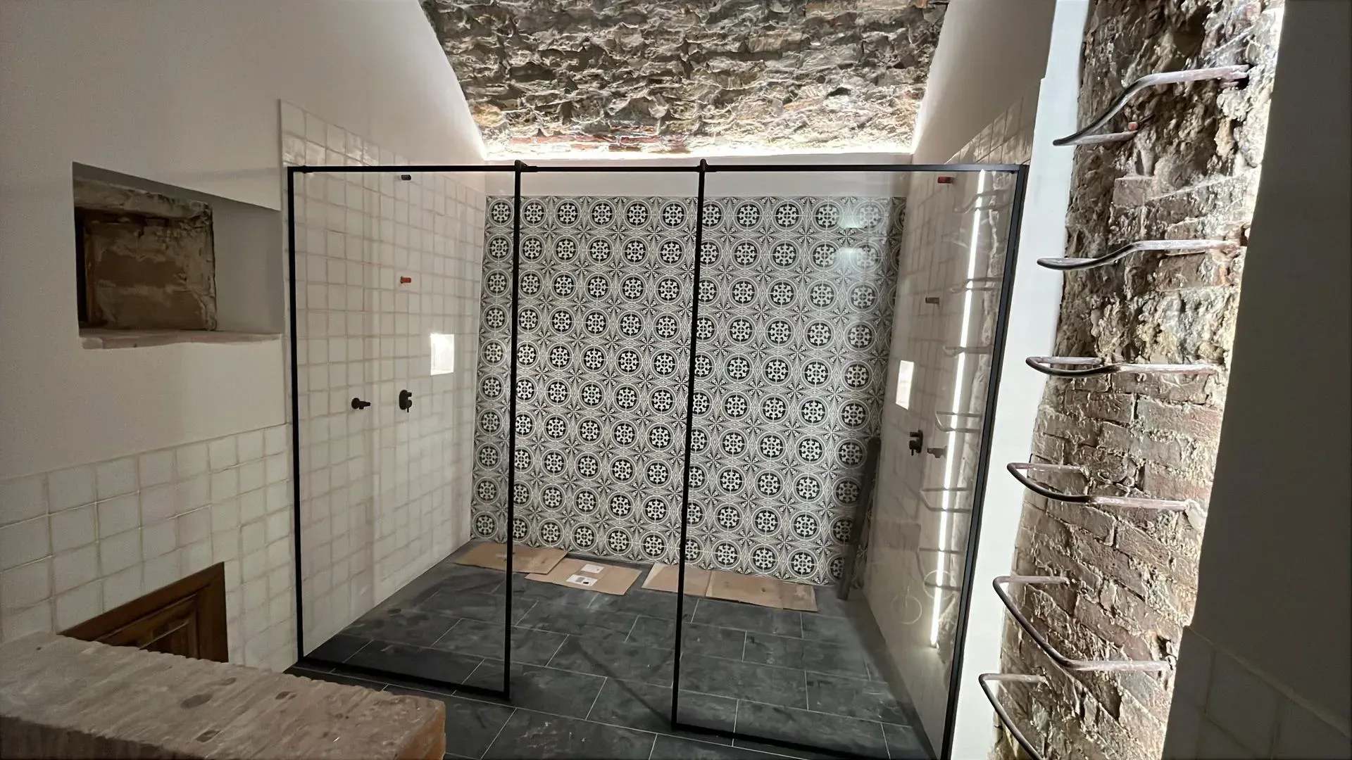 Box doccia interno con pareti piastrellate, porta in vetro decorato e soffitto con finitura in pietra a vista.
