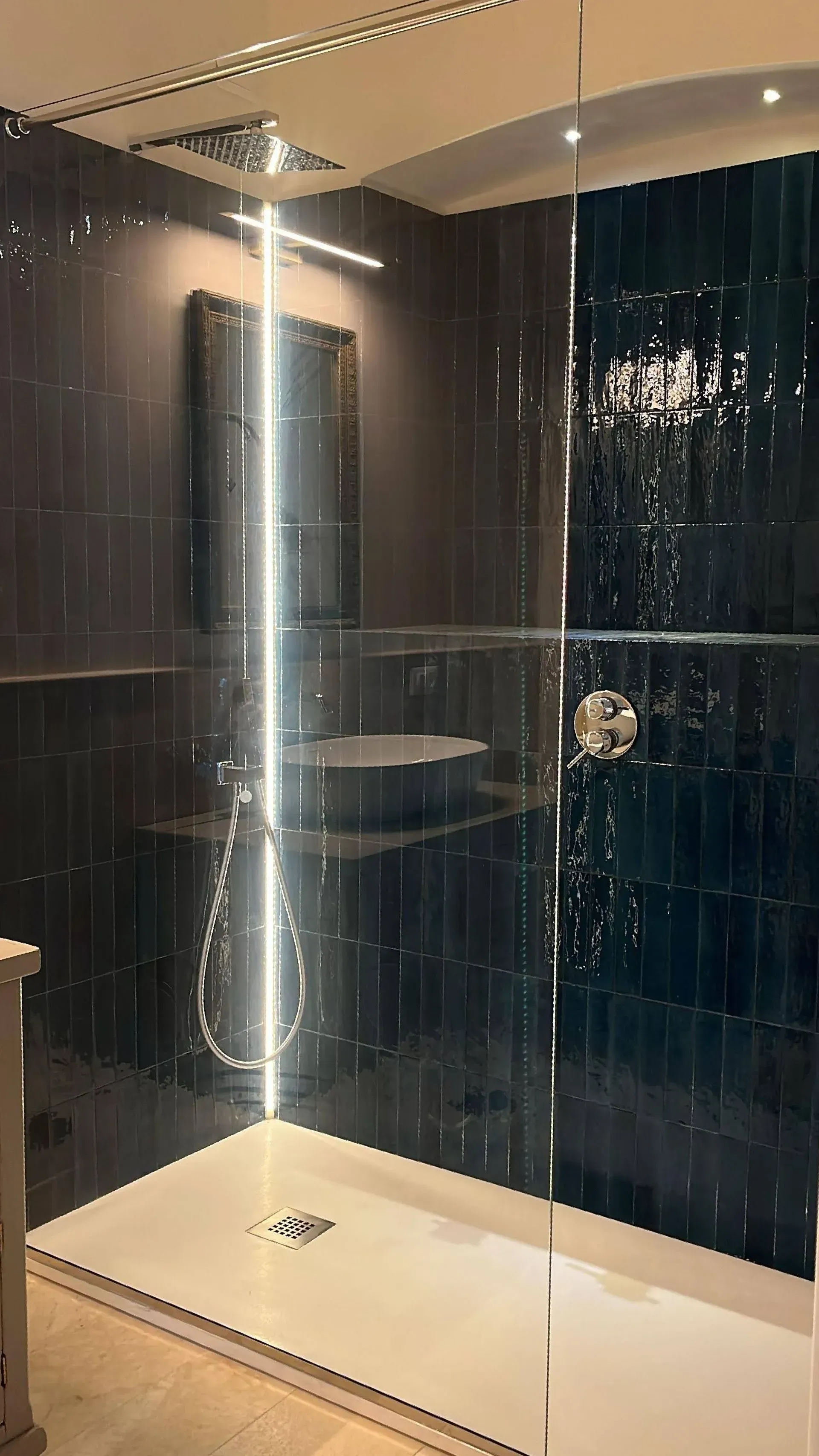 Cabina doccia moderna con box in vetro, pavimento in piastrelle bianche e rivestimento a parete con piastrelle scure a trama ruvida.