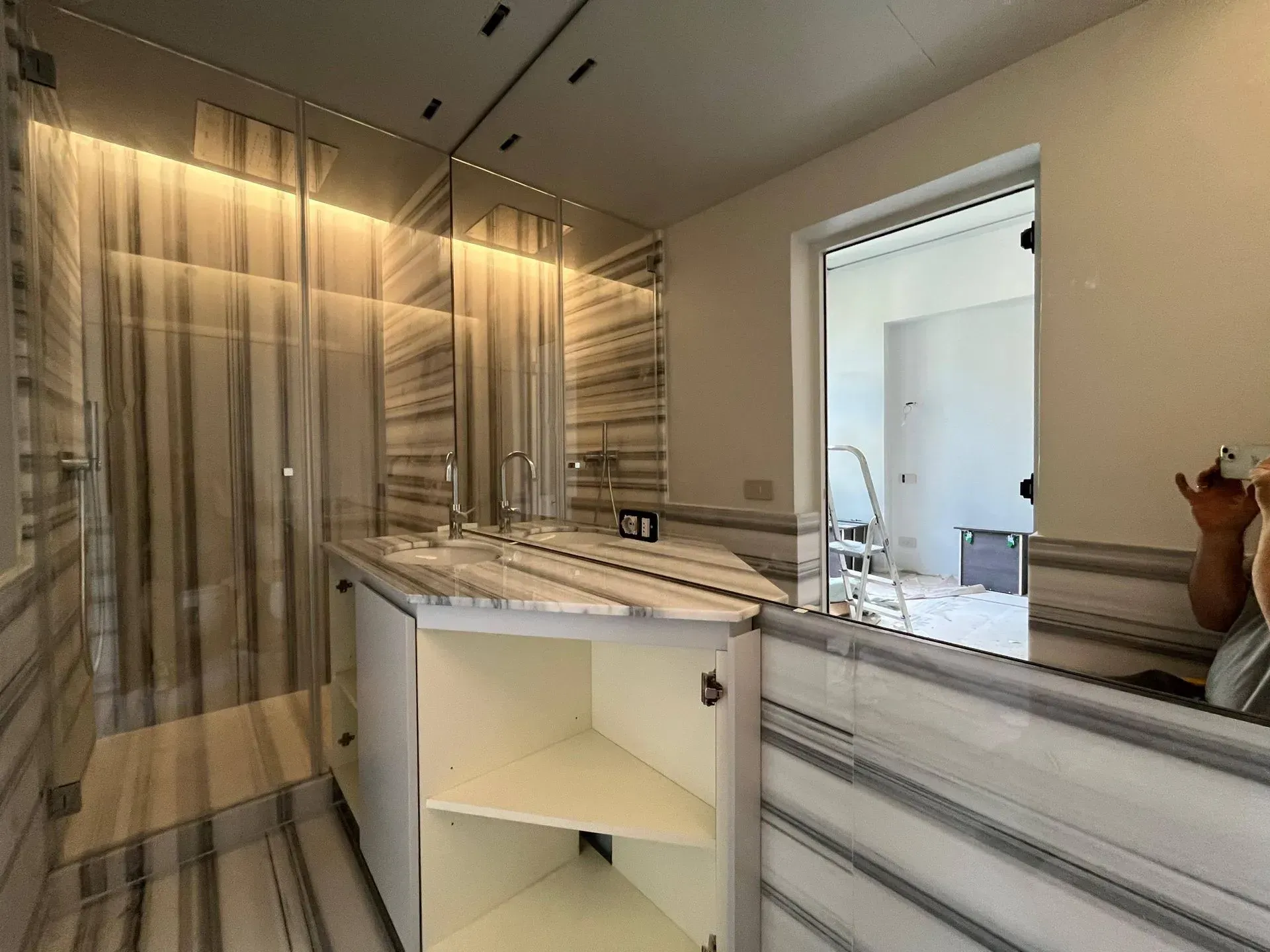 Bagno moderno con lavabo in marmo, ampio specchio, tenda da doccia a righe e porta aperta su un'altra stanza.