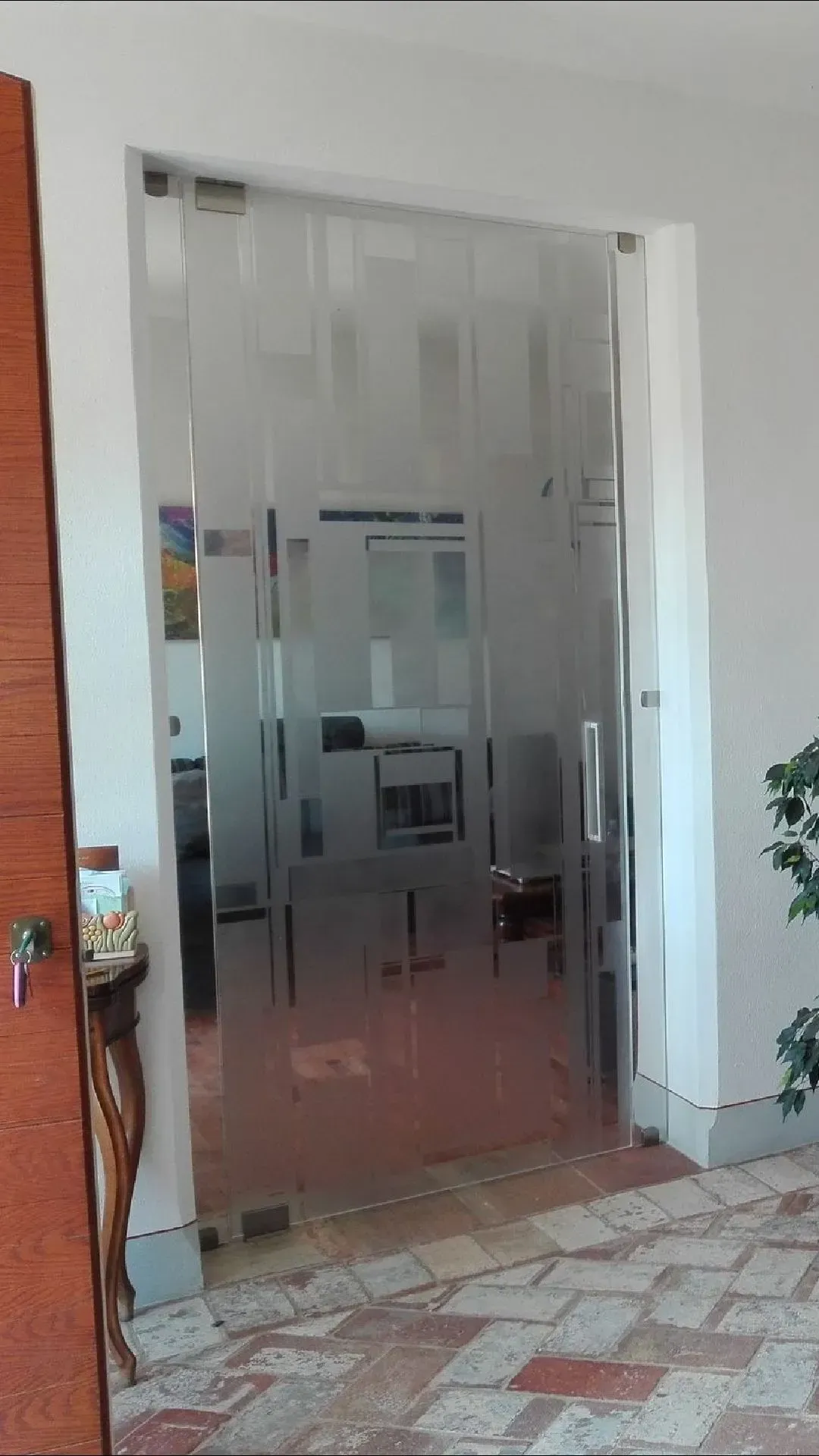 Porta d'ufficio in vetro con strisce verticali satinate in un corridoio bianco con pavimento piastrellato.