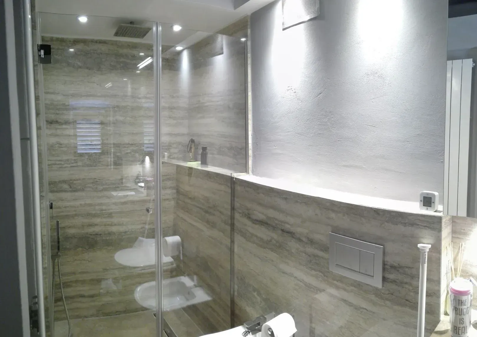 Bagno moderno con doccia in vetro, pareti piastrellate e WC sospeso.