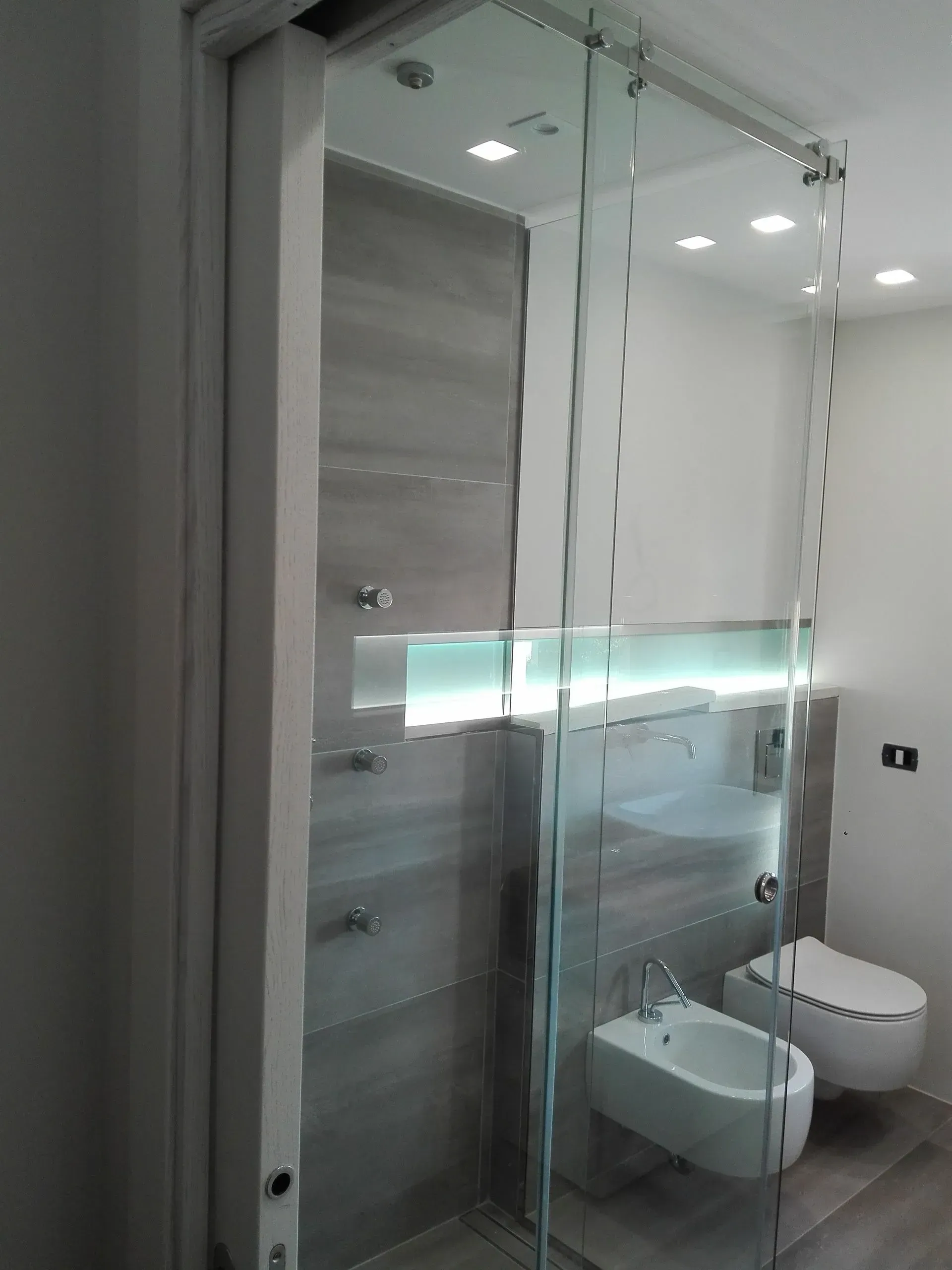 Bagno moderno con box doccia in vetro, lavabo sospeso e WC a parete, nei toni del grigio e del bianco.