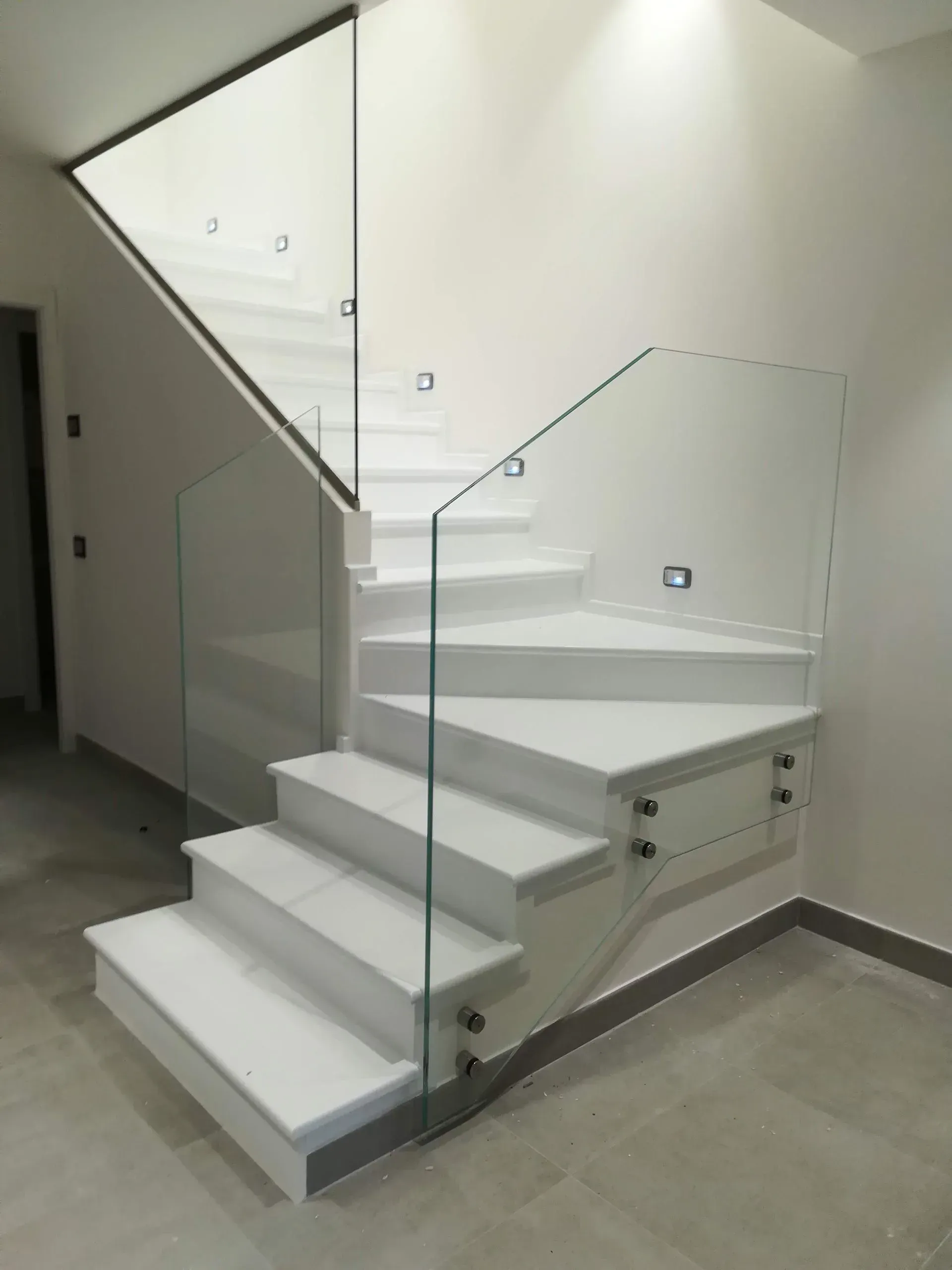 Scala moderna bianca con ringhiera in vetro in un luminoso corridoio interno.