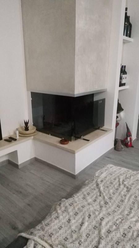 Soggiorno moderno con camino ad angolo, pareti bianche, pavimento grigio e una coperta a fantasia in primo piano.