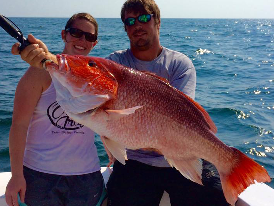 A man and woman on a boat holding a large red fish