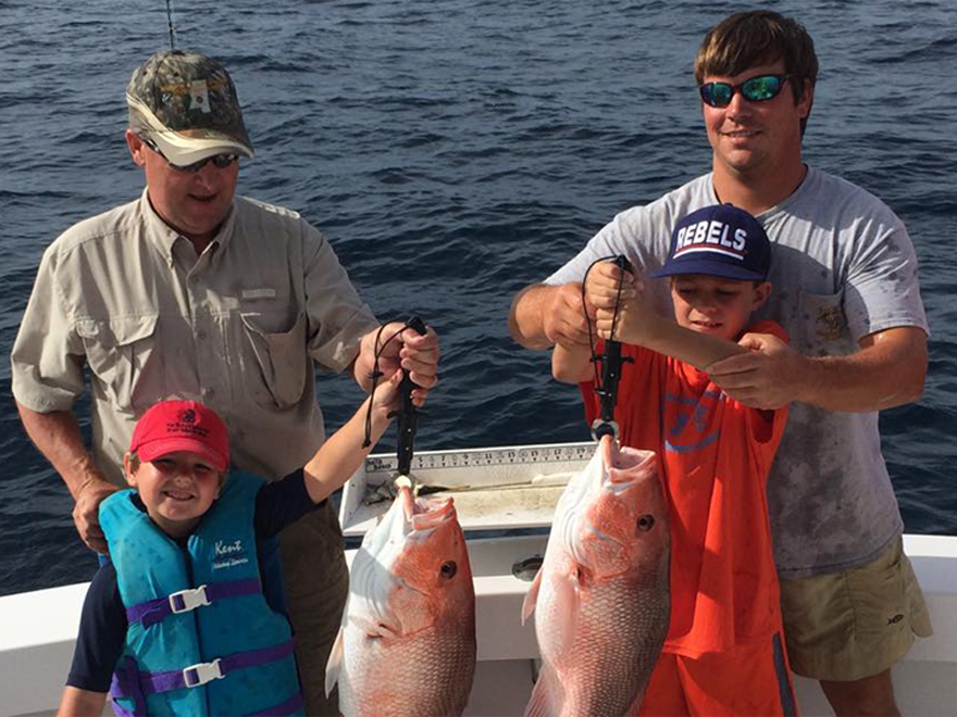 Two men and two children are holding fish on a boat.