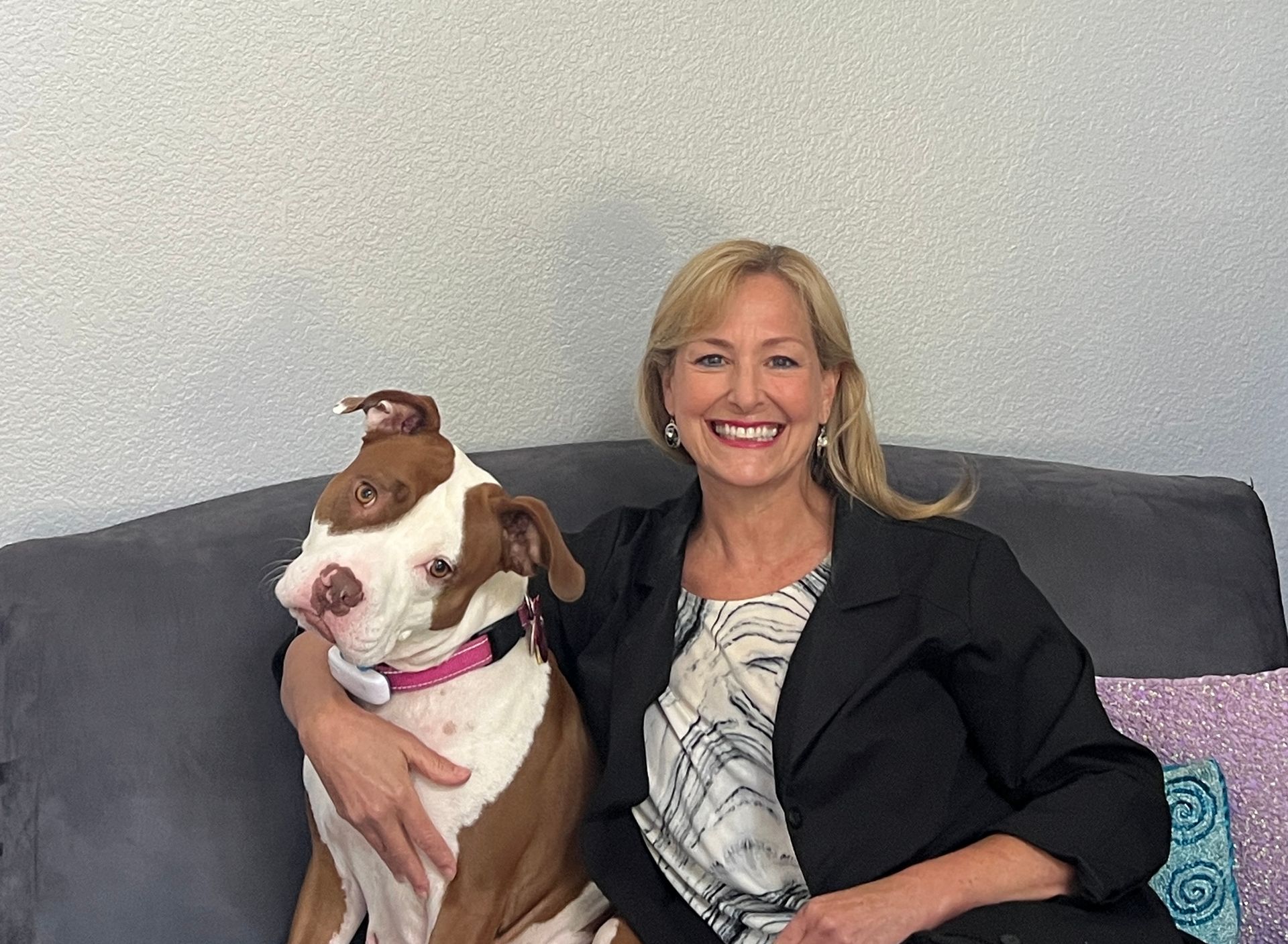 A woman is sitting on a couch holding a brown and white dog.