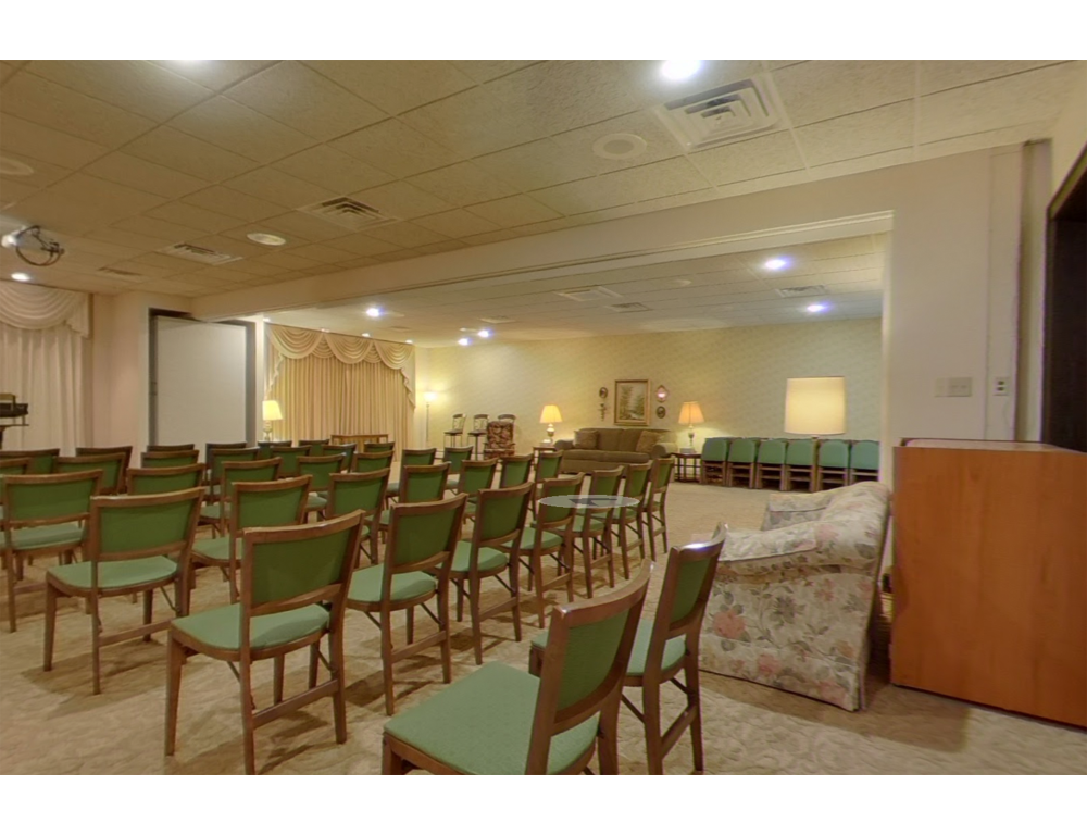 A large hall with rows of green chairs facing a projection screen, beige walls, and soft lighting for an event.