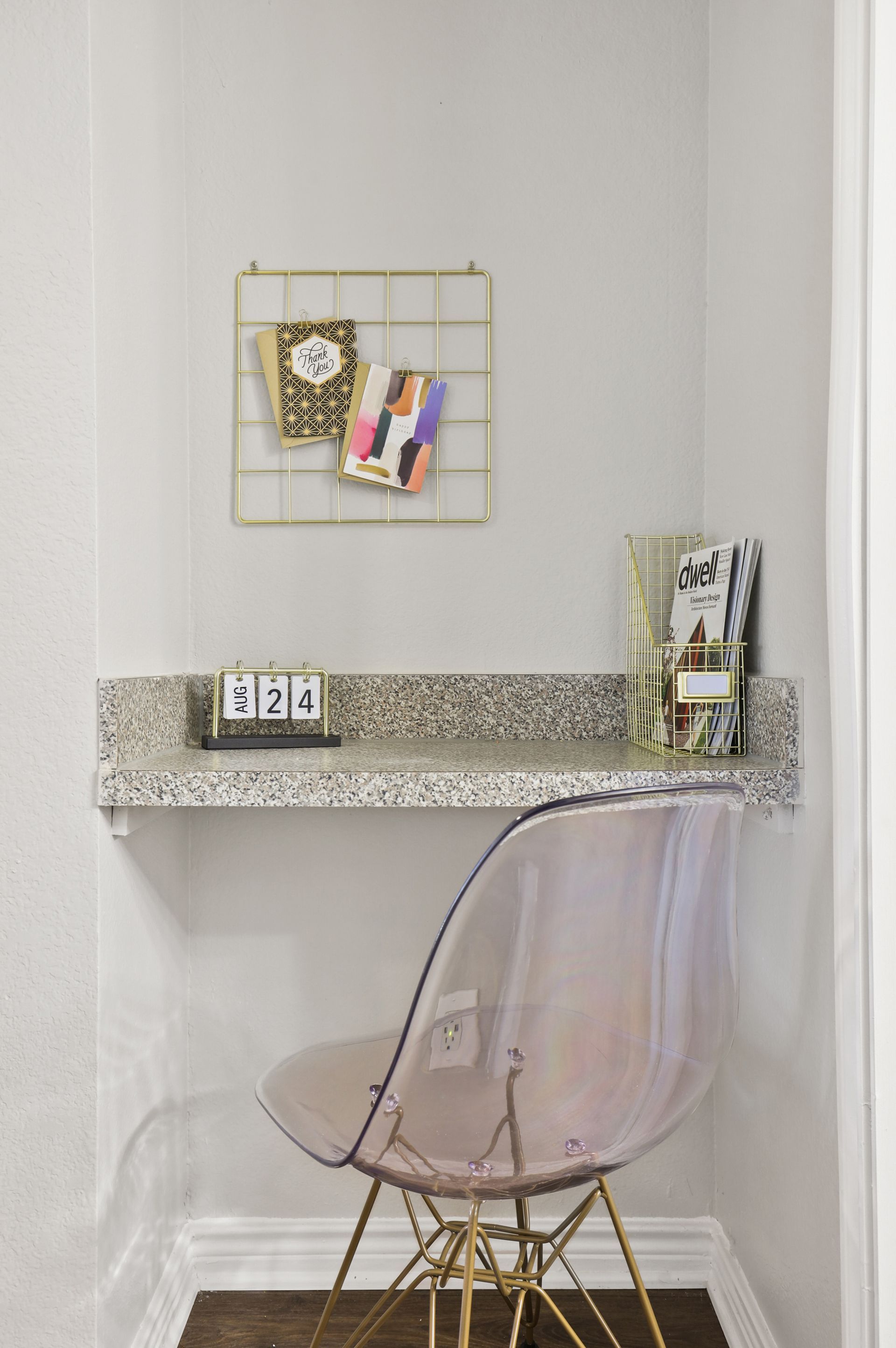 Small desk nook with a floating shelf and clear pink chair. Gold accents, gray walls.