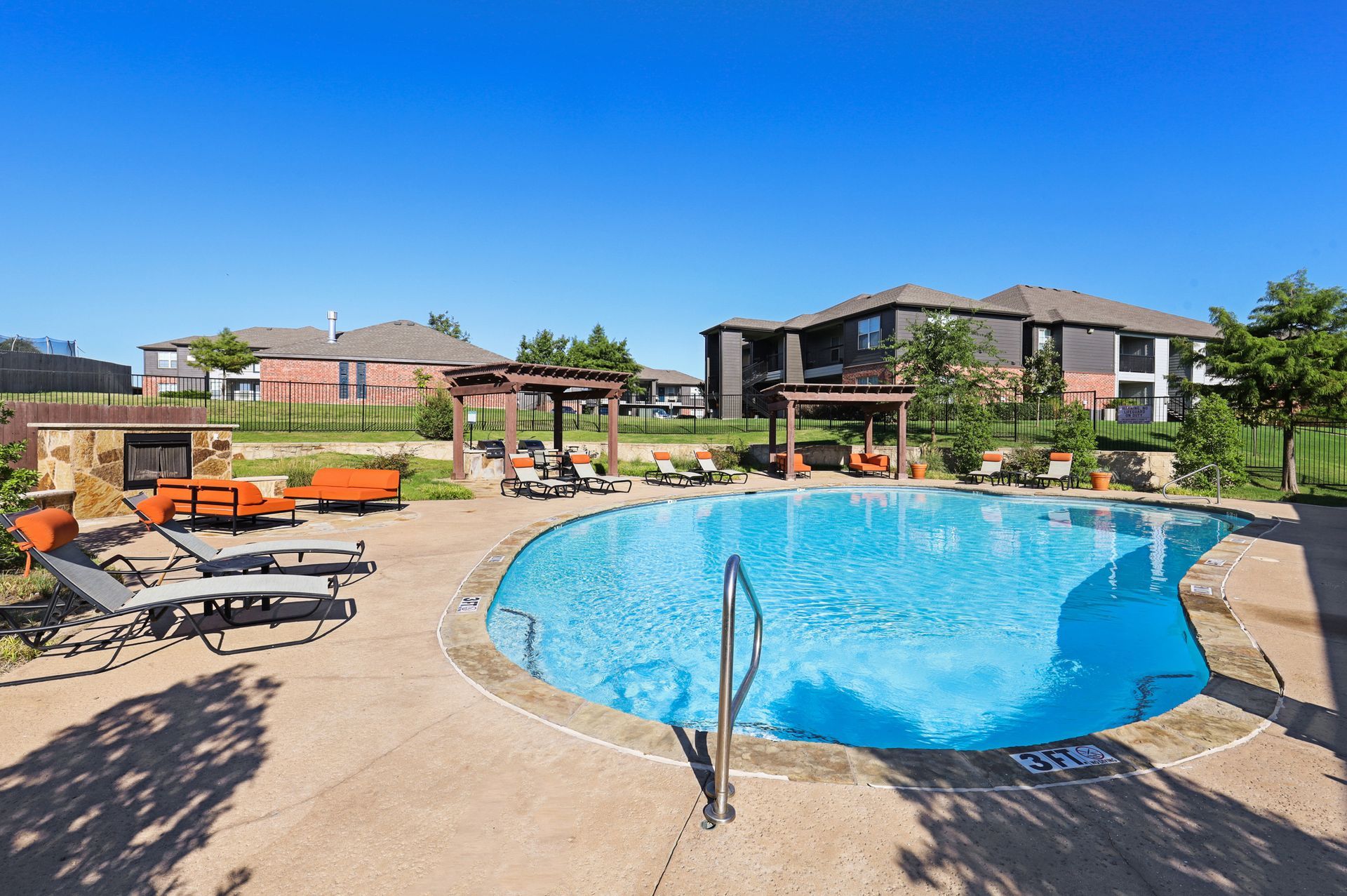 Swimming pool with lounge chairs, pergolas, and apartment buildings on a sunny day.