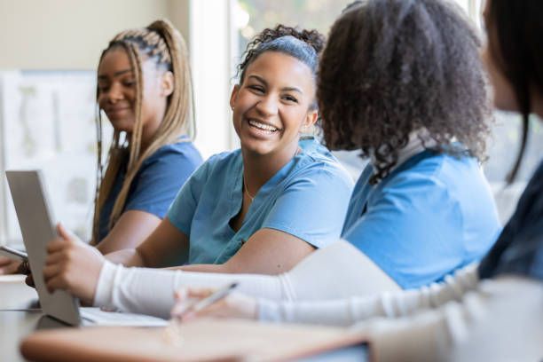 Four medical professionals in blue scrubs at a table, smiling and looking at a tablet and notepad.