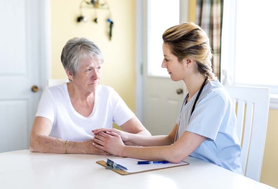 Nurse comforts elderly patient, holding her hands, while sitting at a table.