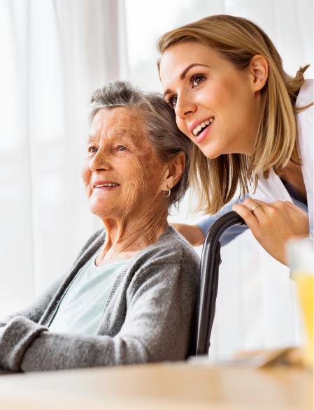 Woman in wheelchair, caregiver smiling, looking out a window.