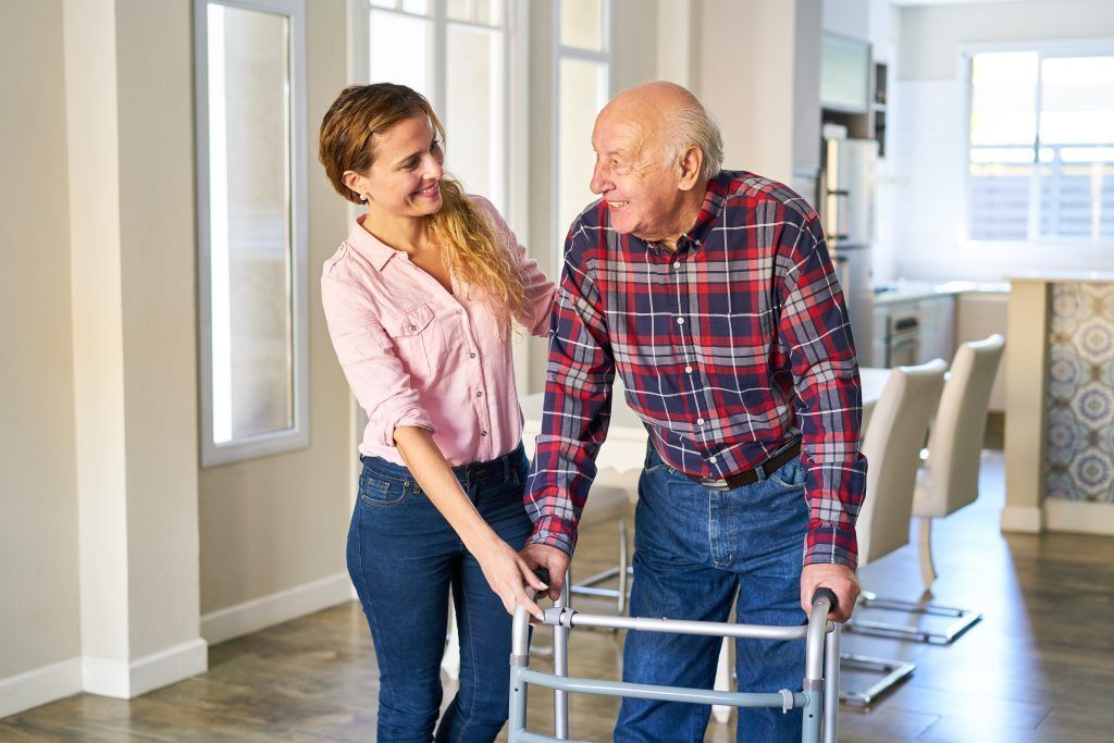 Woman assisting an elderly person with a walker in a well-lit home.
