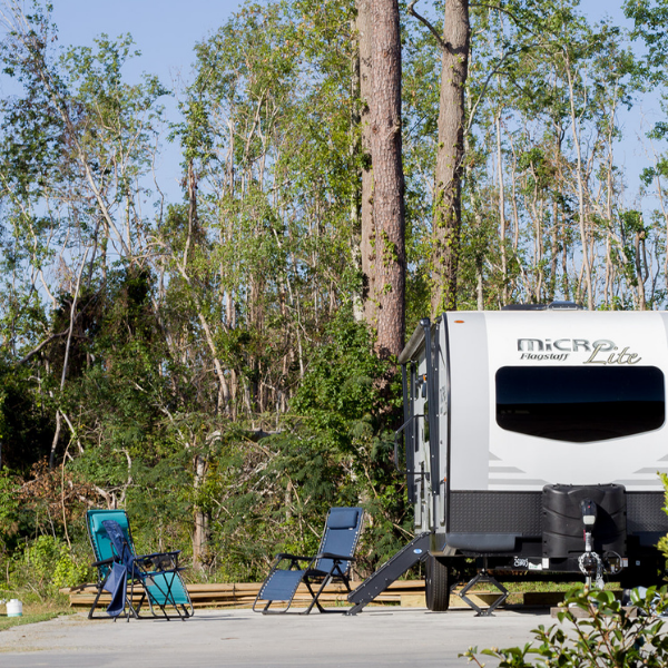 A rv is parked in a parking lot with chairs and trees in the background.