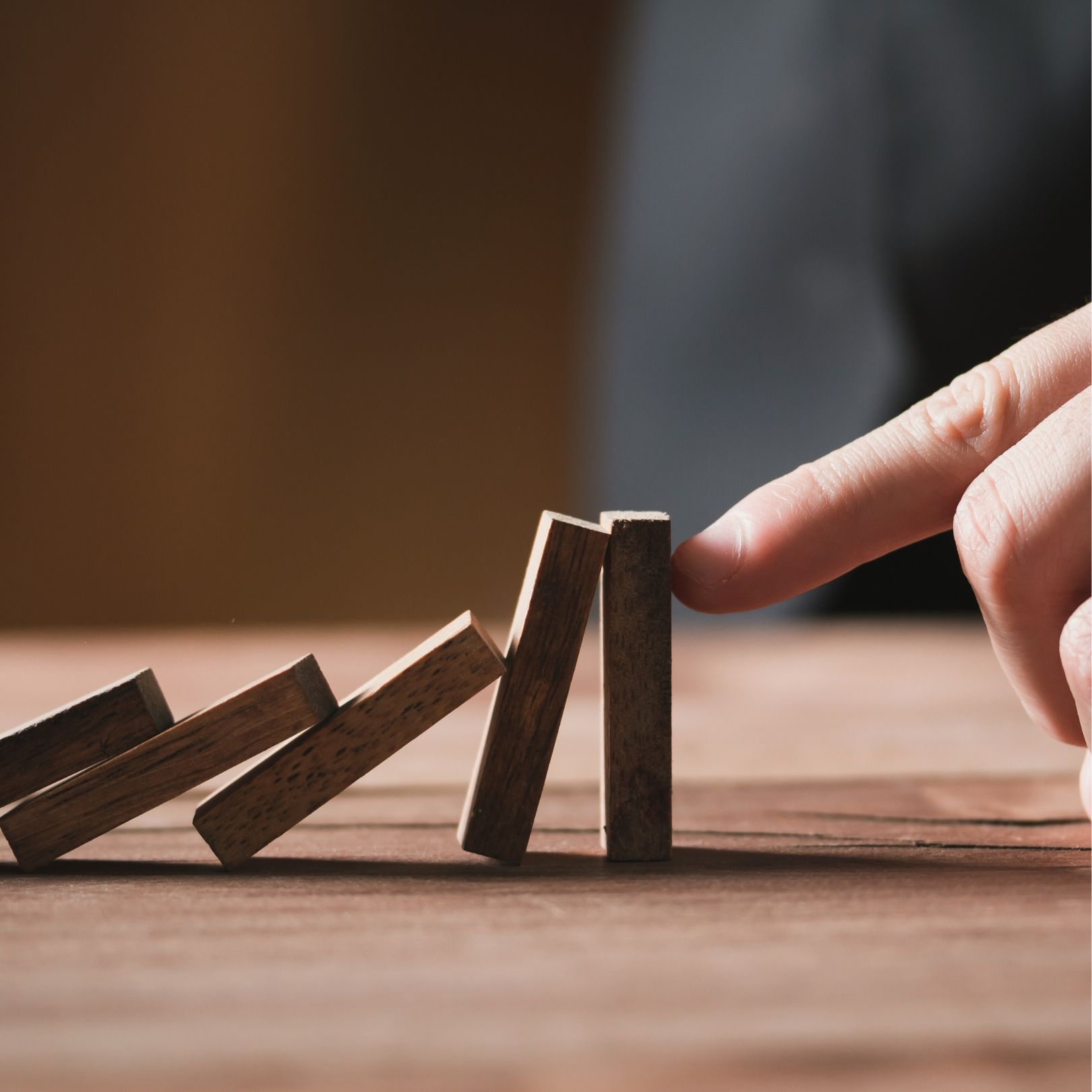 Hand pushing a domino as others stand and fall on a wooden surface