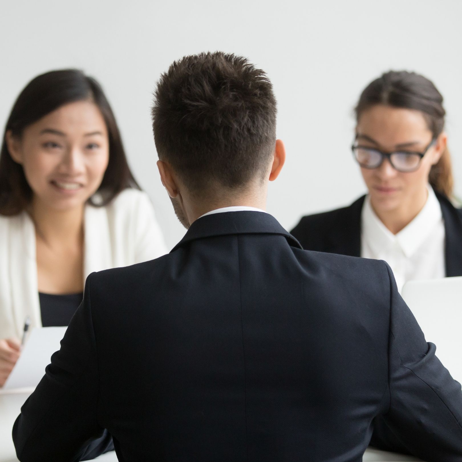 Business meeting with three people seated at a table, one seen from behind facing two colleagues.