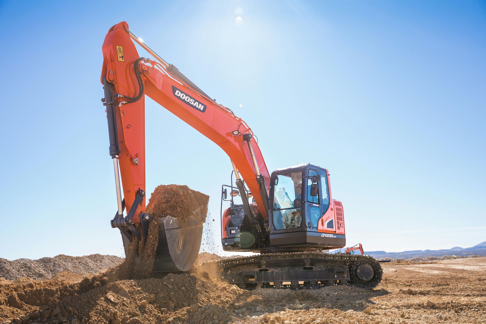 Orange excavator dumping dirt at a construction site under a clear blue sky