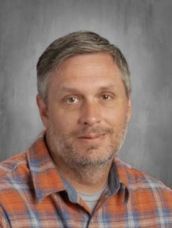 A man with a beard and a plaid shirt is posing for a picture.