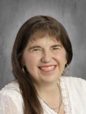 A woman in a white shirt and necklace is smiling for the camera.