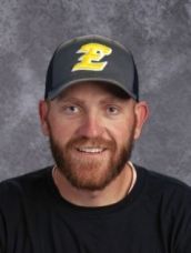 A man with a beard is wearing a baseball cap and smiling.