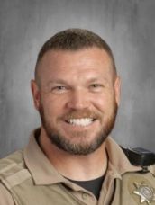 A man with a beard and a sheriff 's badge is smiling for the camera.