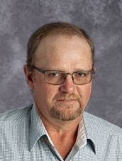 A man with glasses and a beard is wearing a blue shirt.