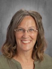 A woman wearing glasses and a green shirt is smiling for the camera.
