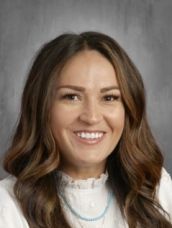 A woman with long hair and a necklace is smiling for a picture.