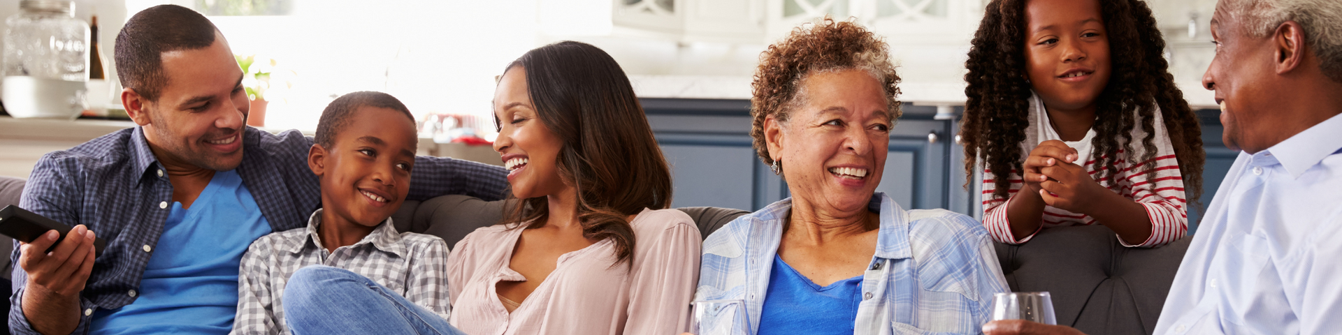 Five people sitting together on a couch, smiling and chatting in a bright living room.
