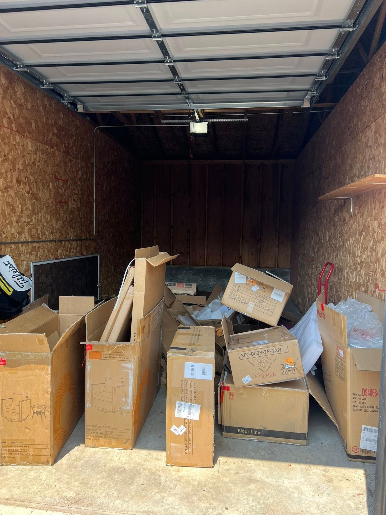 An open storage unit with several cardboard boxes scattered on the floor and against the wooden interior walls.
