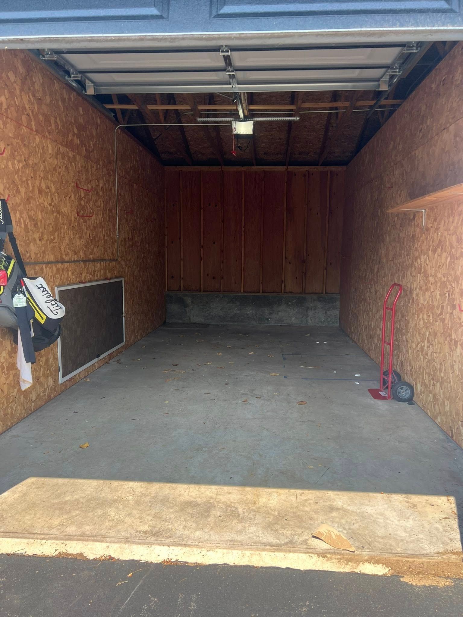 Empty garage interior with particleboard walls, concrete floor, overhead door, and a few items leaning against the walls.