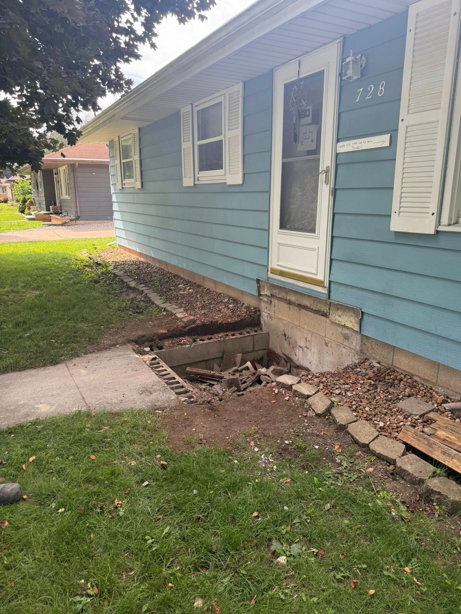 Blue house exterior showing a missing concrete porch step and a deep, exposed gap in the foundation.